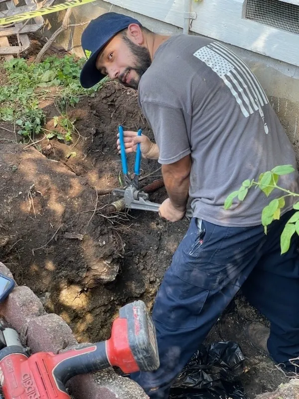 A man in grey shirt digging with blue tools.