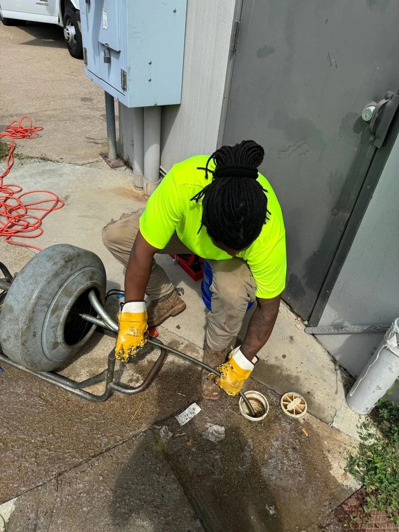 A man in yellow shirt and gloves working on pipe.