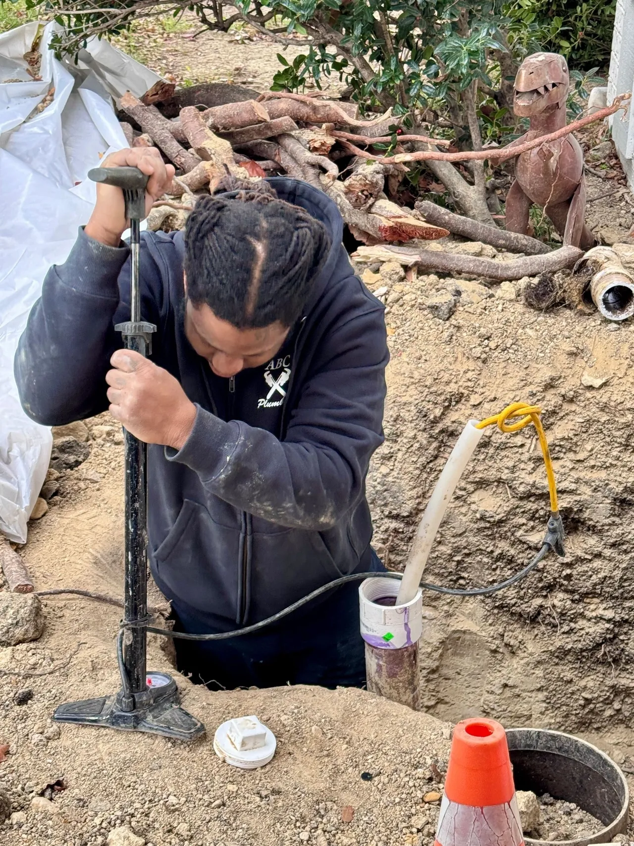 A man in black jacket fixing pipe on dirt ground.