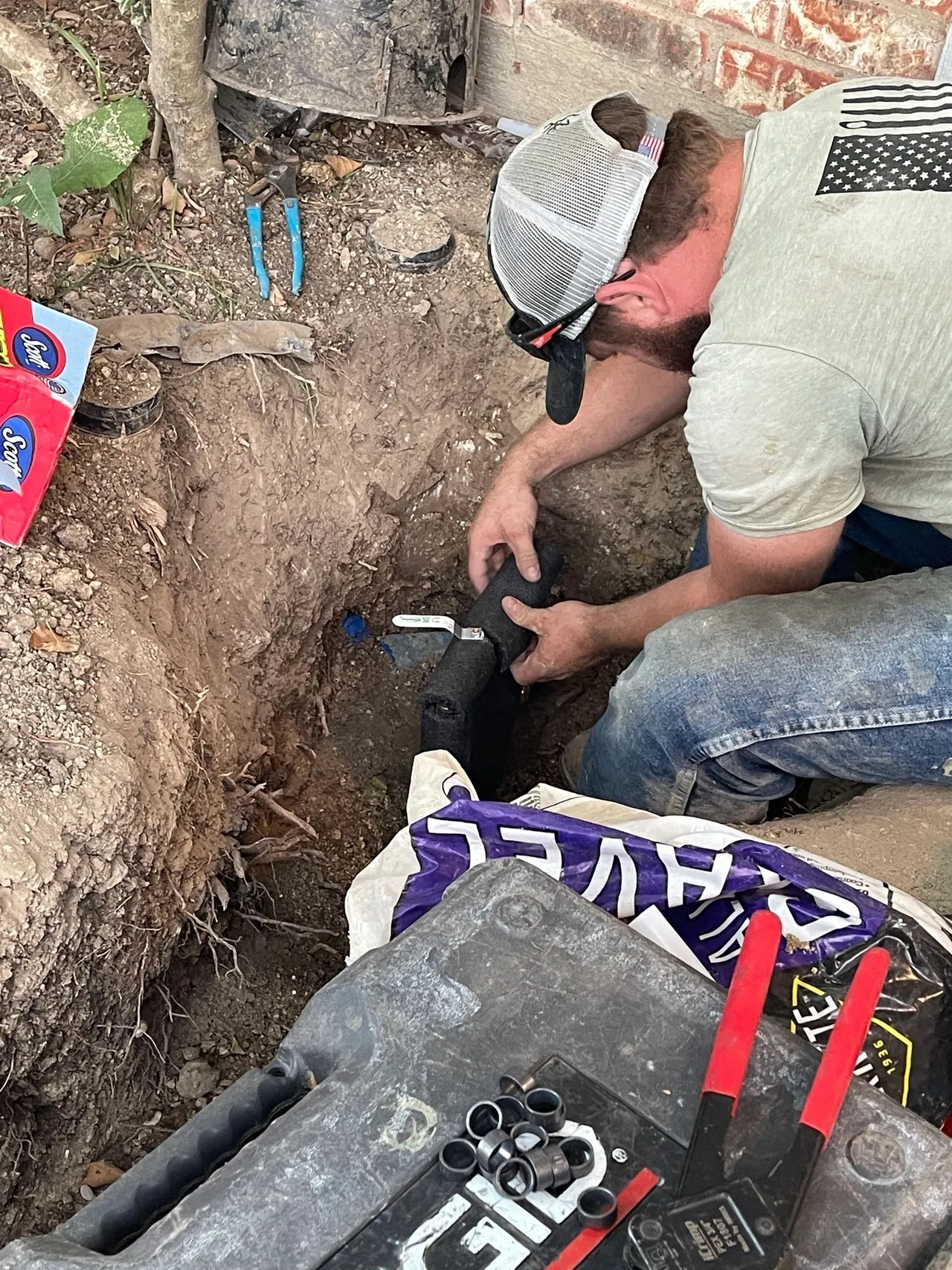 A man in white shirt and jeans working on a hole.