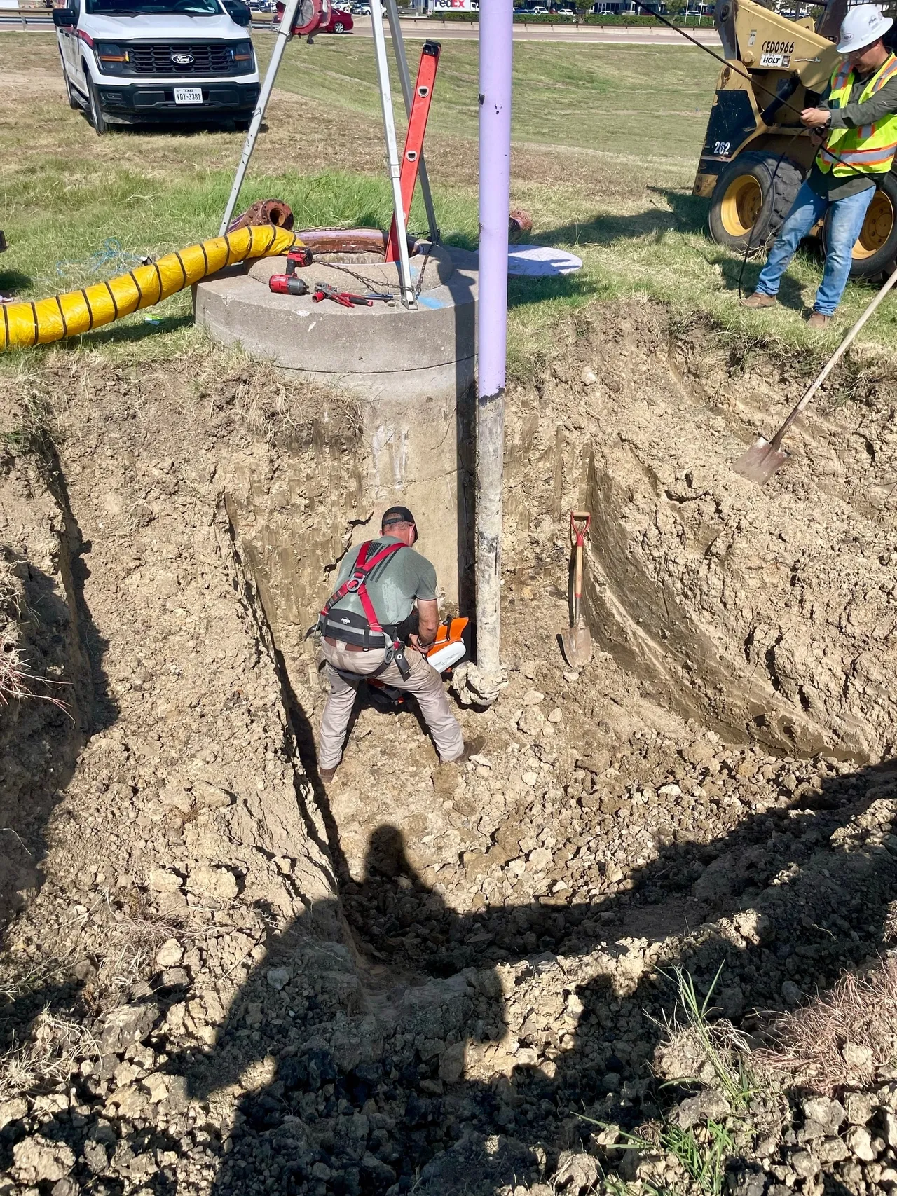 A man in grey shirt and yellow hard hat working on a hole.