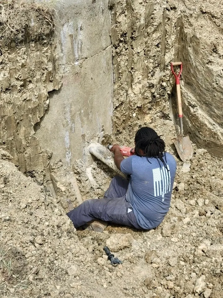 A man sitting on the ground in front of a rock wall.