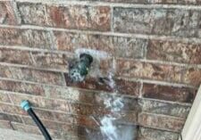 A water hose is spraying out of the side of a brick wall.